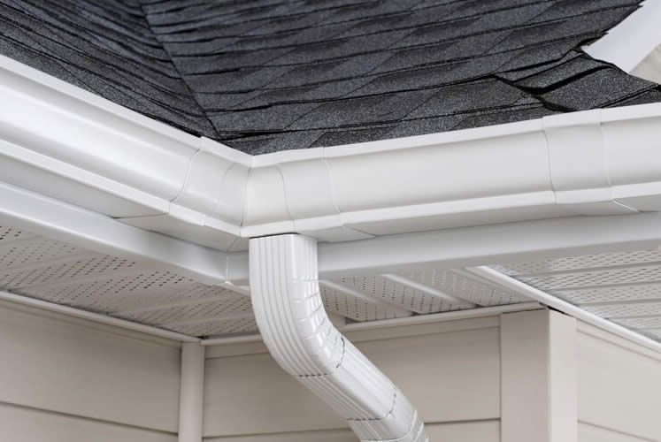 A white gutter on the side of a house with a black roof.