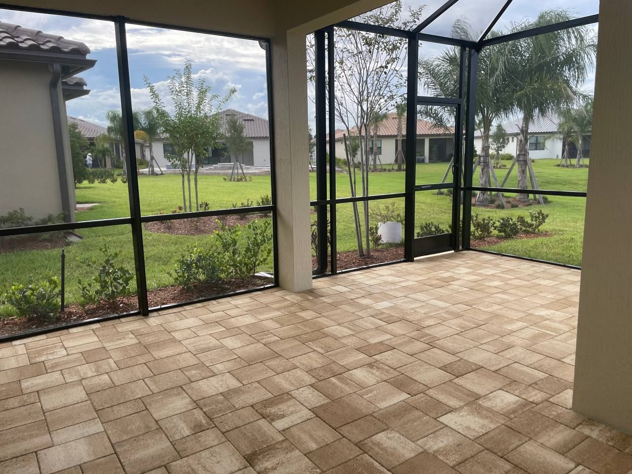 A screened in porch with a brick house in the background.