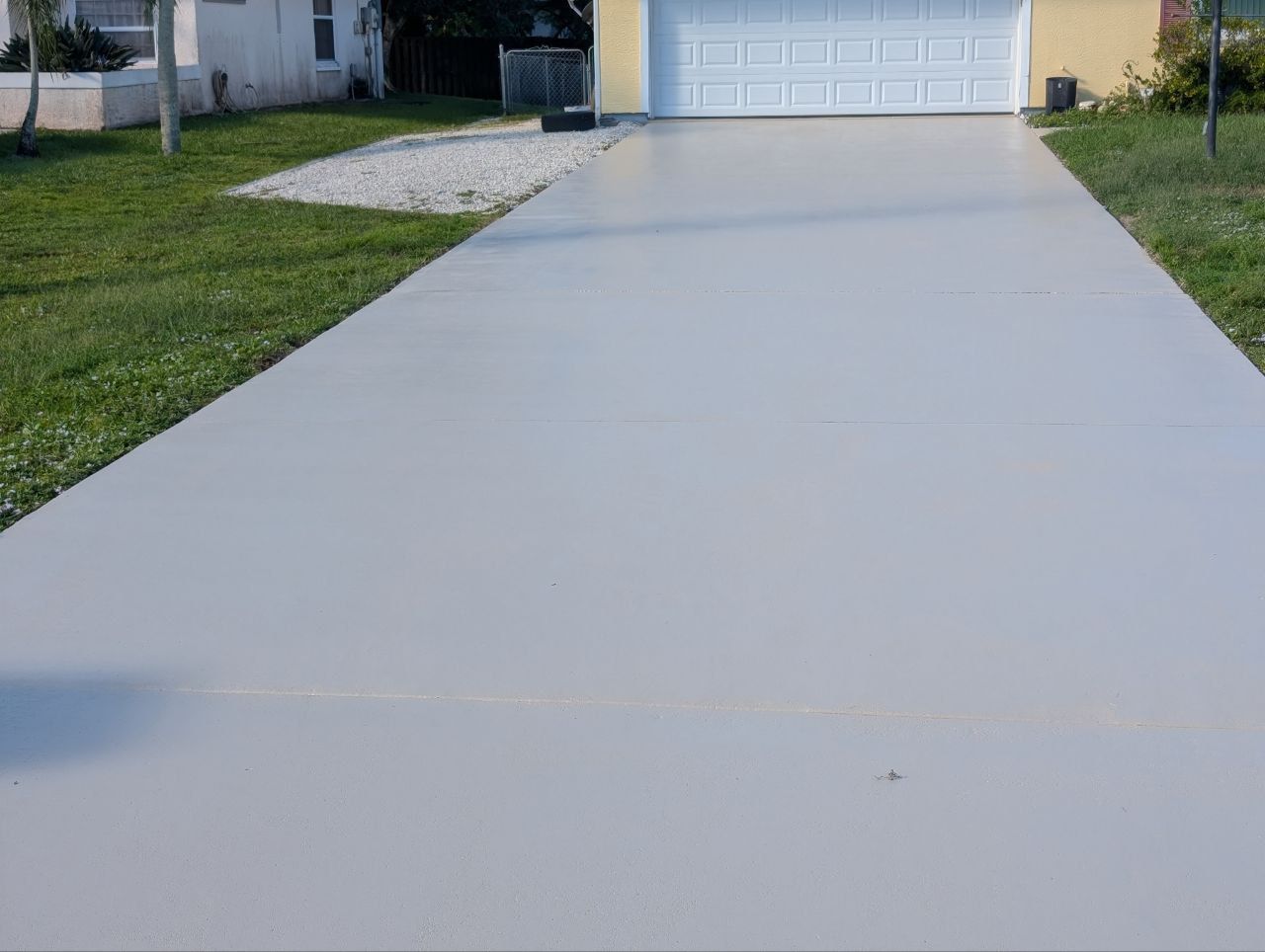 Light gray concrete driveway leading to a white garage door, bordered by green grass.