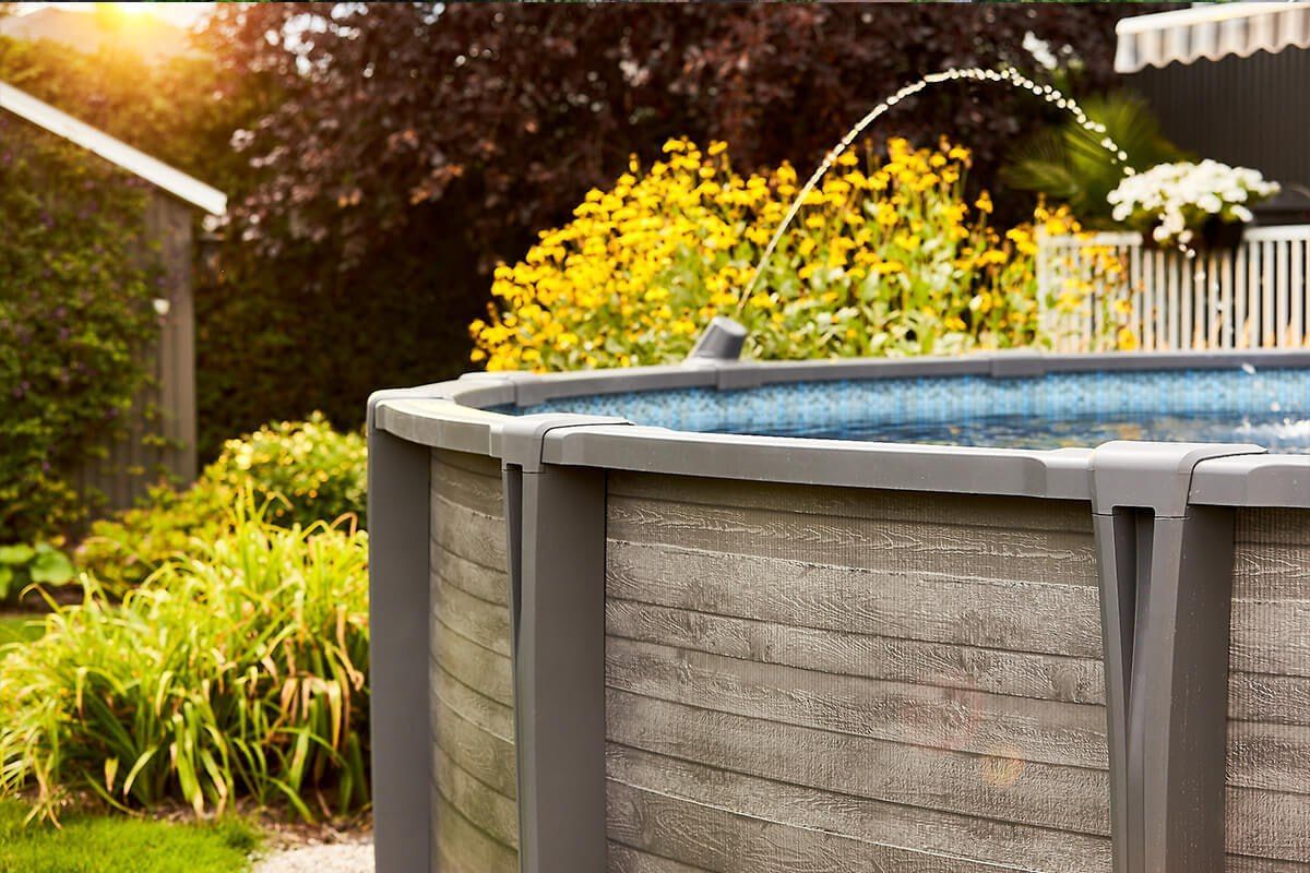 Above-ground pool with integrated fountain feature and native landscaping installed by Right Way Enclosures in Sebastian, Florida.