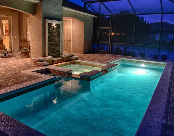 Custom concrete pool with LED lighting, integrated spa, and stacked-stone waterfall feature at twilight in Palm Bay, Florida.