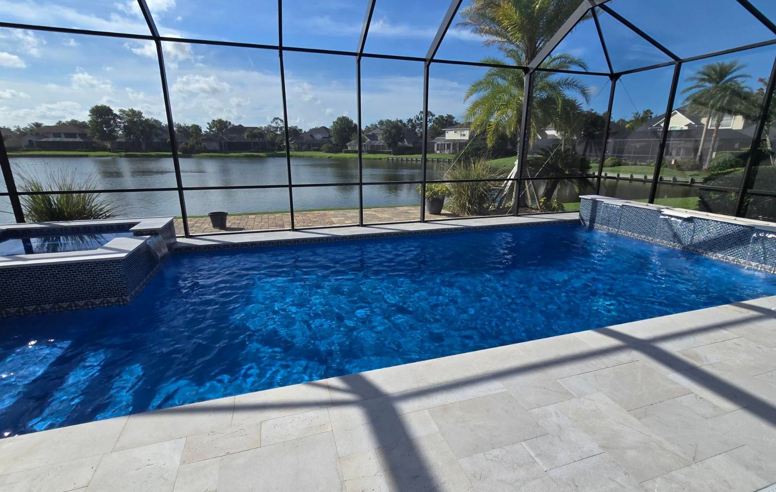 Lakefront custom concrete pool with integrated spa and travertine deck by Right Way Enclosures in Melbourne, Florida.