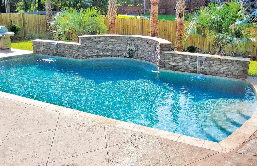Freeform custom concrete pool with stacked-stone waterfall and stamped concrete deck by Right Way Enclosures in Indian River County, Florida.