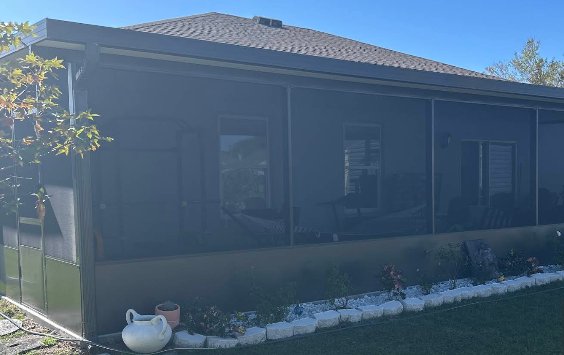 Single-story house with dark exterior, tiled roof, and flower bed along the front lawn.