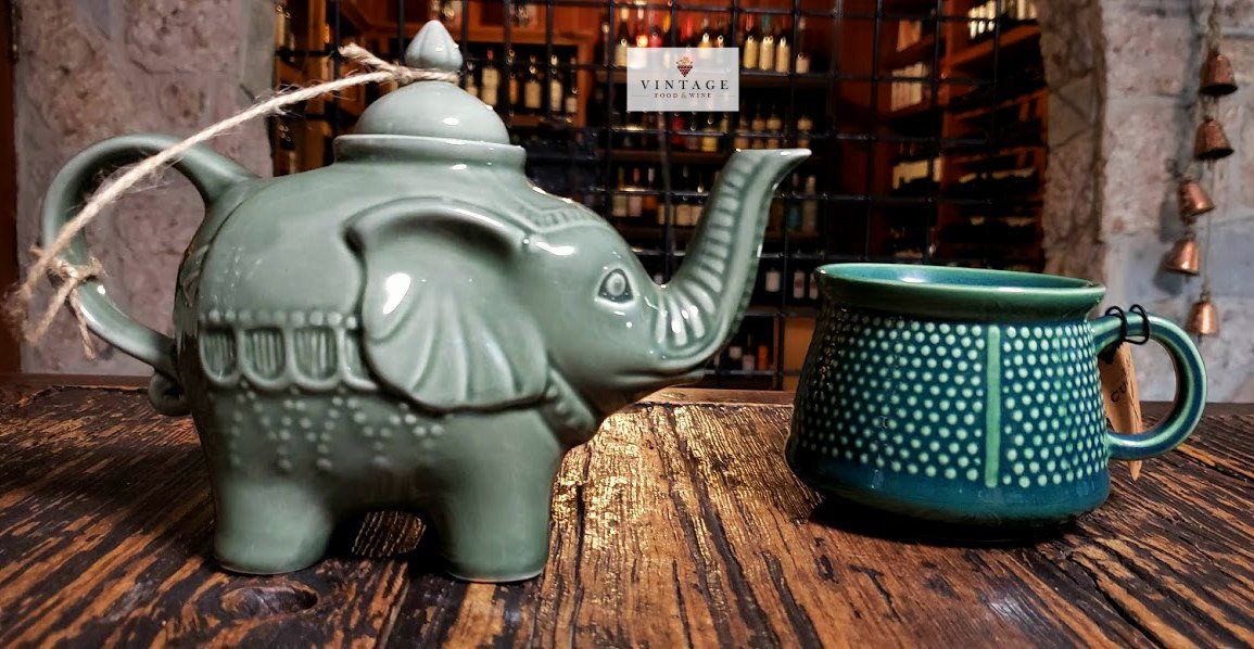 Una tetera con forma de elefante y una taza sobre una mesa de madera.