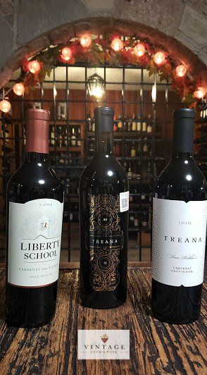 Hay tres botellas de vino sobre una mesa de madera.