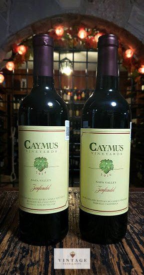 Dos botellas de vino Caymus están sobre una mesa de madera.