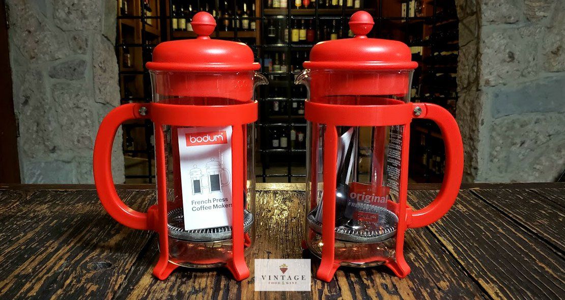 Dos cafeteras de prensa francesa de color rojo están sobre una mesa de madera.