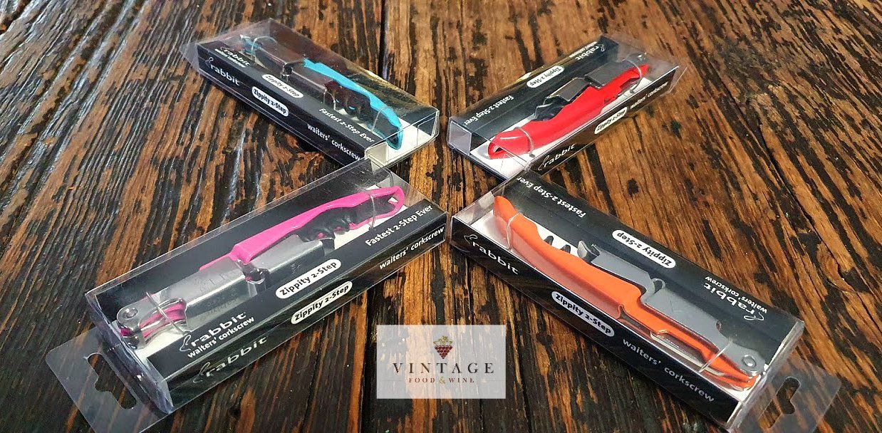 Cuatro abridores de vino de diferentes colores están sobre una mesa de madera.