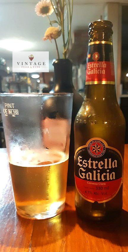 Una botella de cerveza Estrella Galicia junto a un vaso de cerveza.