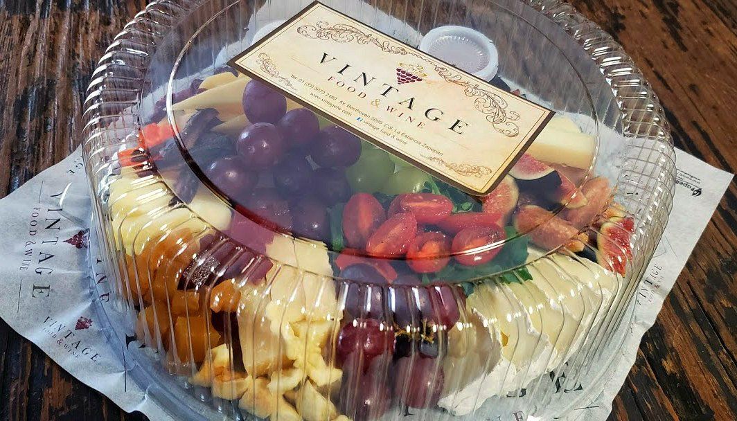 Un recipiente de plástico lleno de fruta y queso sobre una mesa de madera.