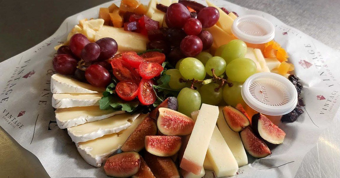 Un plato de queso, uvas, higos y tomates sobre una mesa.