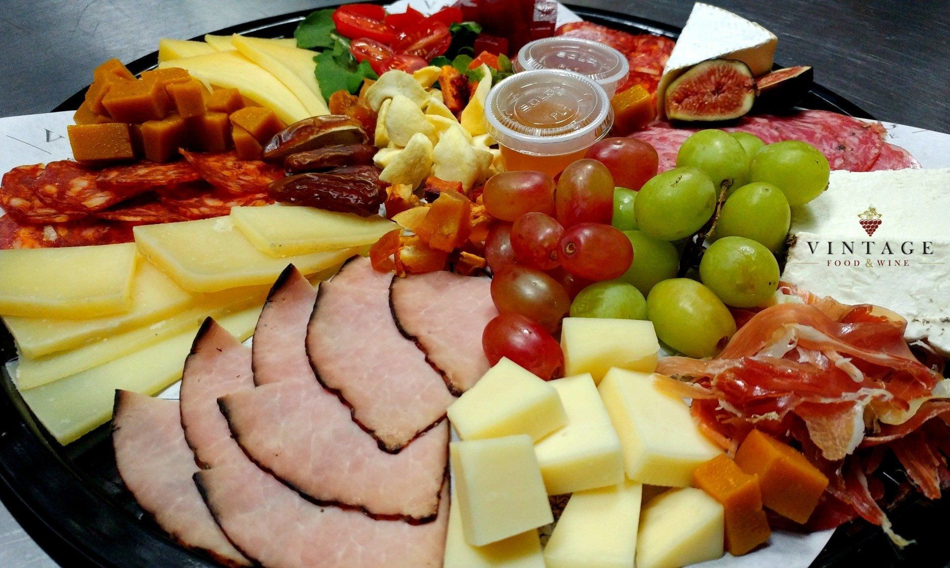 Una bandeja de carnes, quesos, uvas y nueces sobre una mesa.