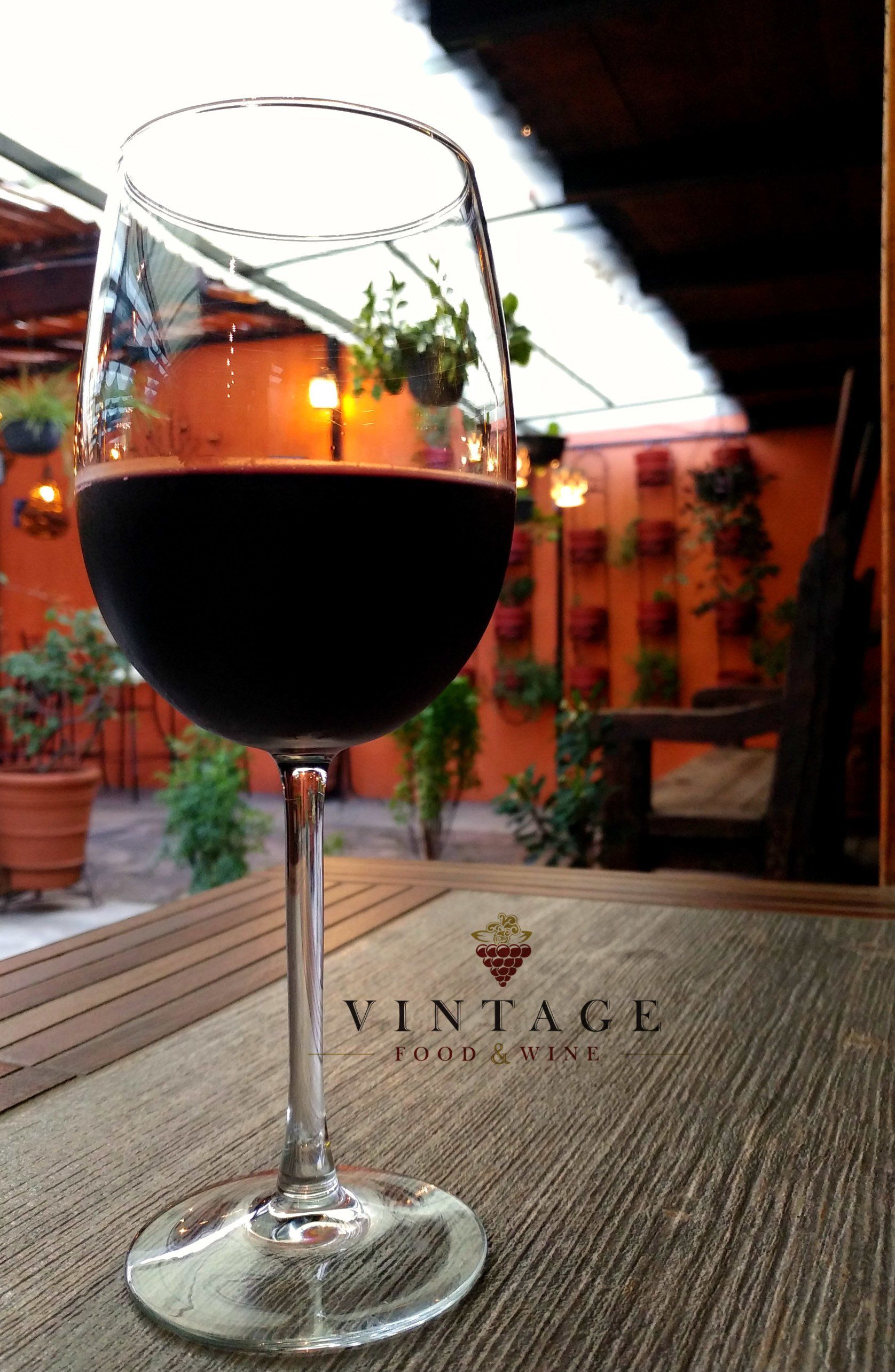 Una copa de vino reposa sobre una mesa de madera delante de un cartel vintage.