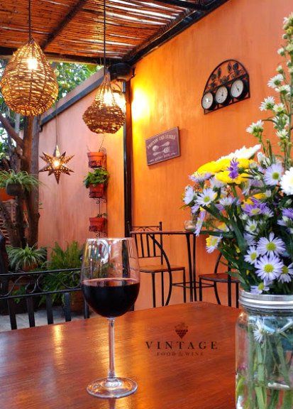 Una copa de vino reposa sobre una mesa delante de un jarrón de flores.