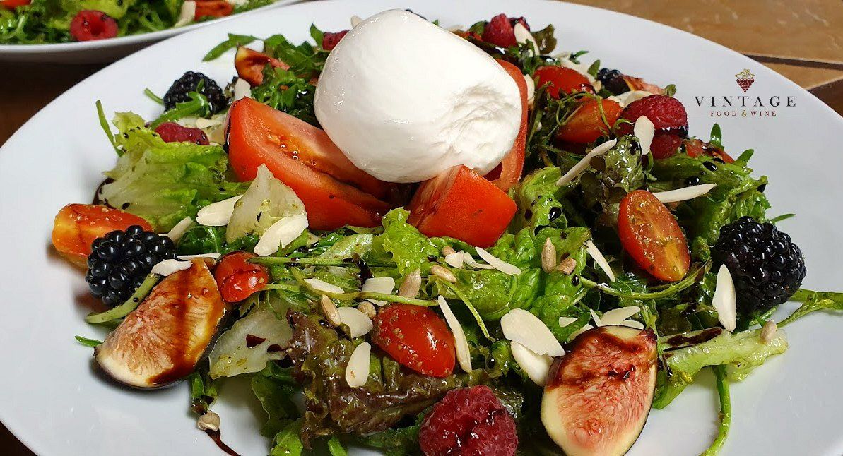 Una ensalada con tomates, higos, almendras y mozzarella en un plato blanco.