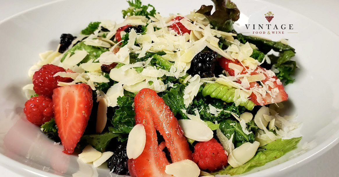Una ensalada con fresas, frambuesas, almendras y queso en un plato blanco.