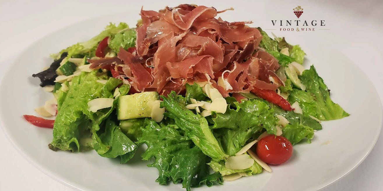 Un plato blanco cubierto con una ensalada con lechuga, tomates y jamón.