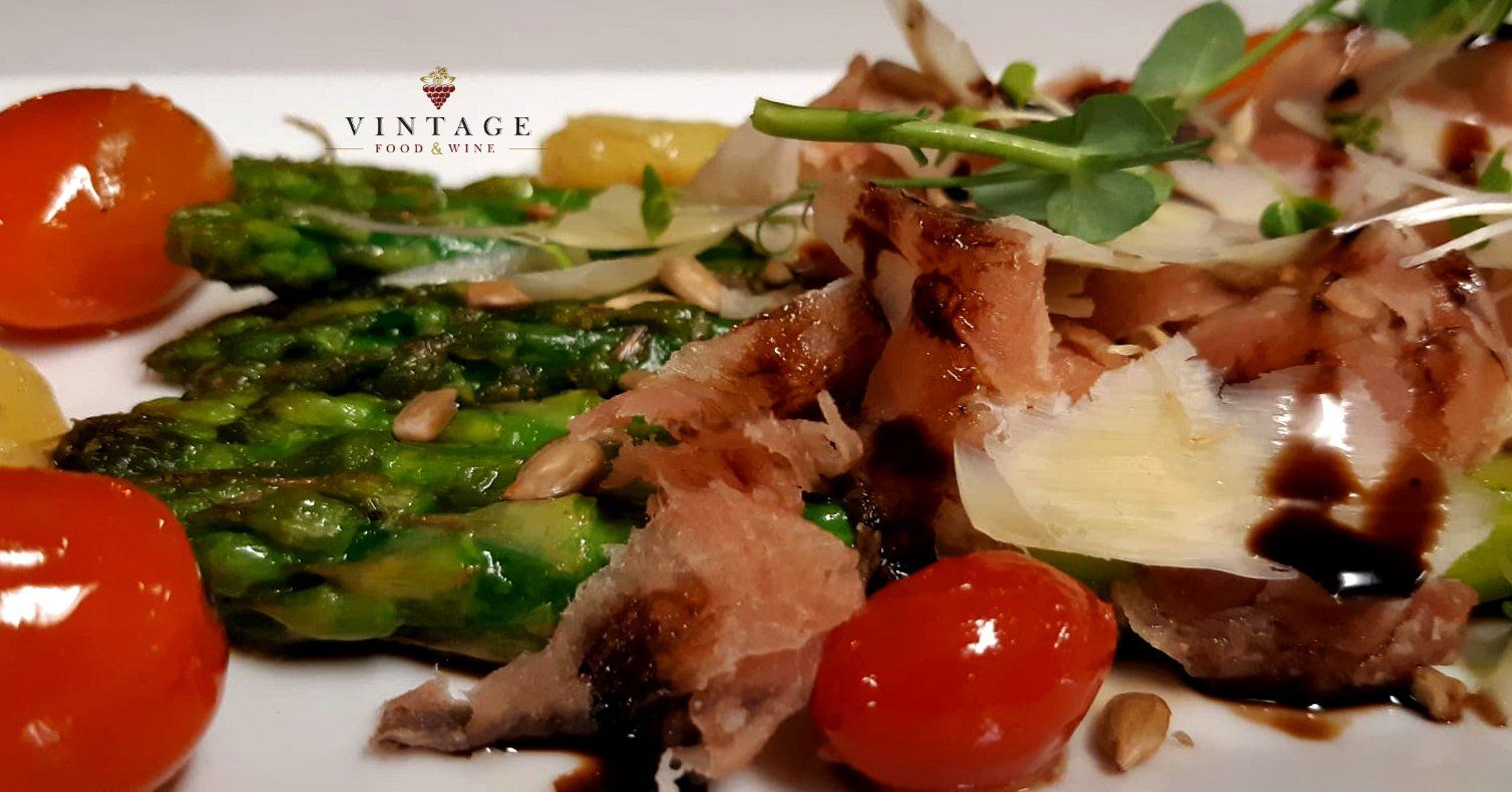 Un plato blanco cubierto con espárragos, tomates y carne.