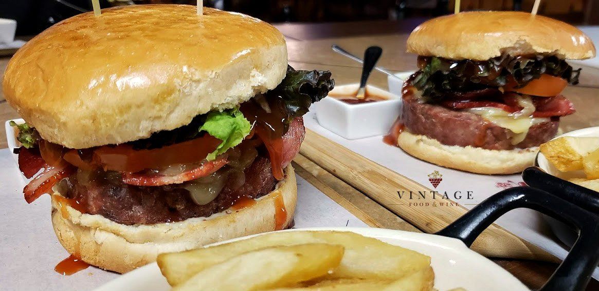 Hay dos hamburguesas en una mesa al lado de un plato de patatas fritas.