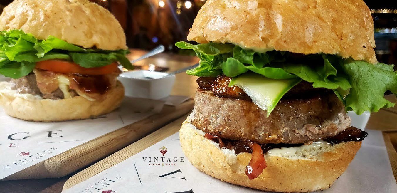 Dos hamburguesas están colocadas sobre una tabla de cortar de madera sobre una mesa.