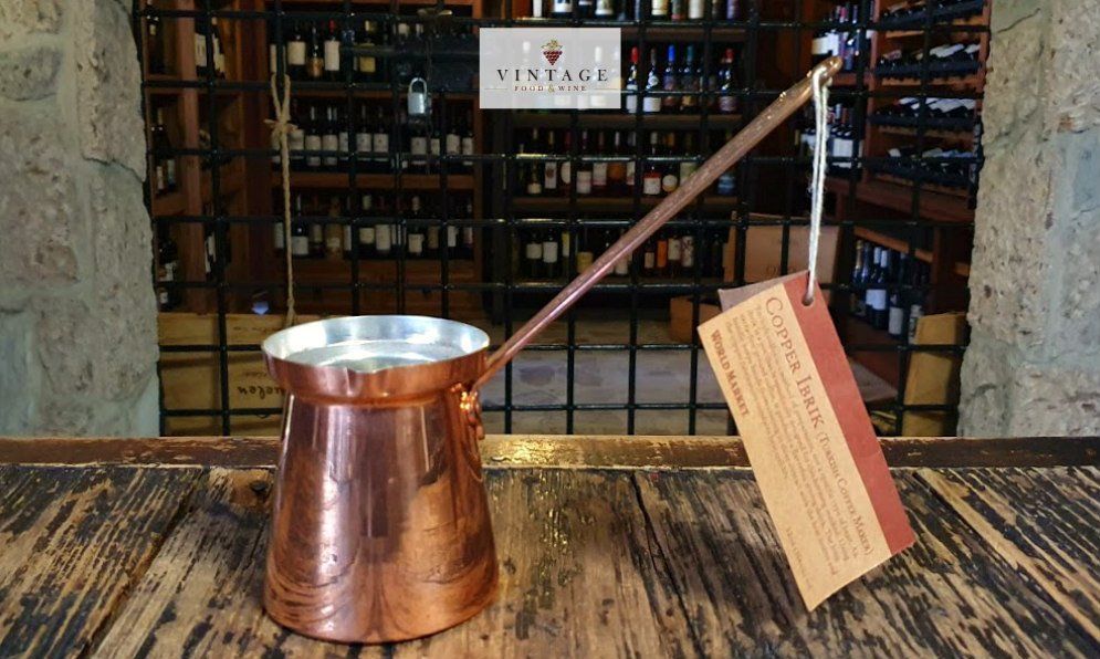 Una olla de cobre con mango de madera está sobre una mesa de madera.