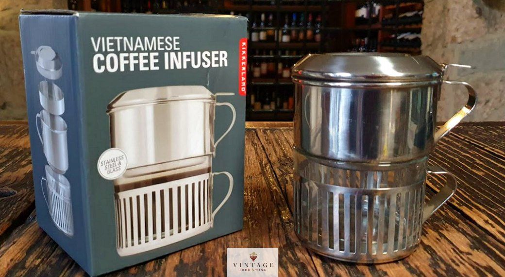 Un infusor de café vietnamita está sobre una mesa de madera al lado de una caja.