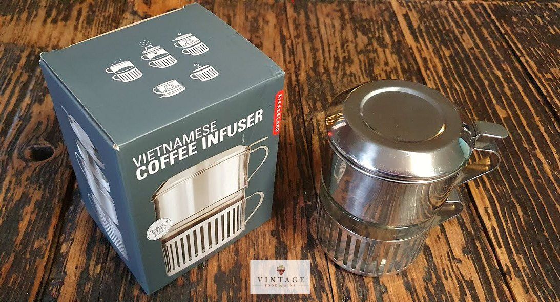 Una cafetera infusora se encuentra encima de una mesa de madera al lado de una caja.