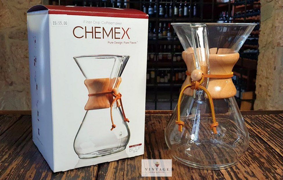 Una cafetera Chemex está sobre una mesa de madera al lado de su caja.