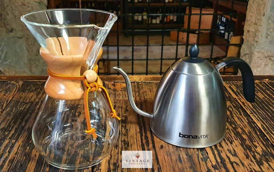 Una cafetera de cristal y una tetera de acero inoxidable están sobre una mesa de madera.