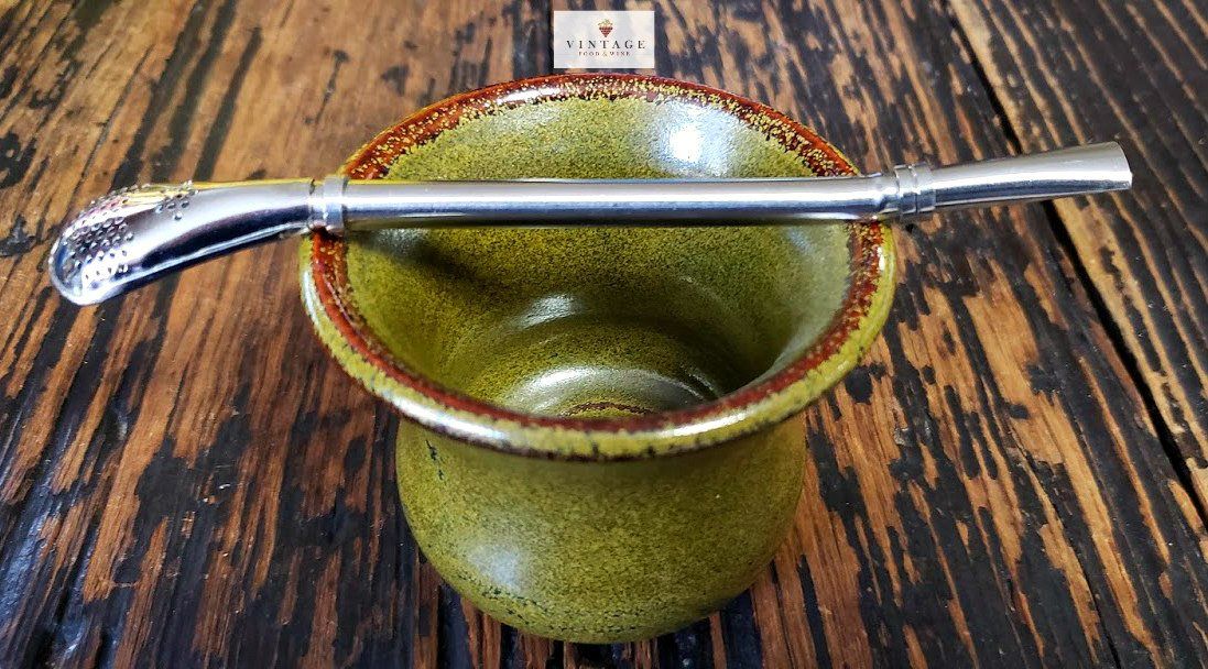 Un recipiente verde con una pajita de metal dentro está sobre una mesa de madera.