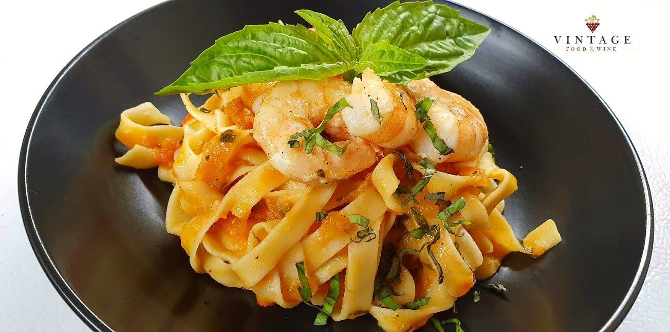 Un primer plano de un plato de pasta con camarones y albahaca sobre una mesa.