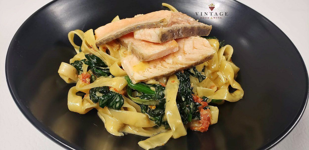 Un primer plano de un plato de pasta con salmón y espinacas.