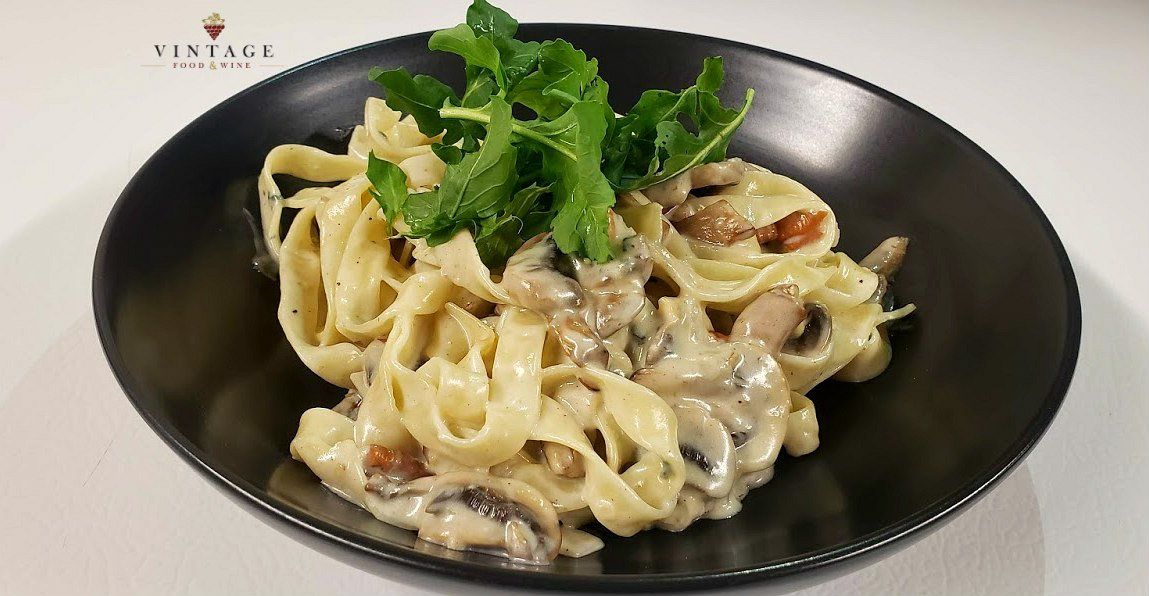 Un plato negro cubierto con pasta y champiñones sobre una mesa.