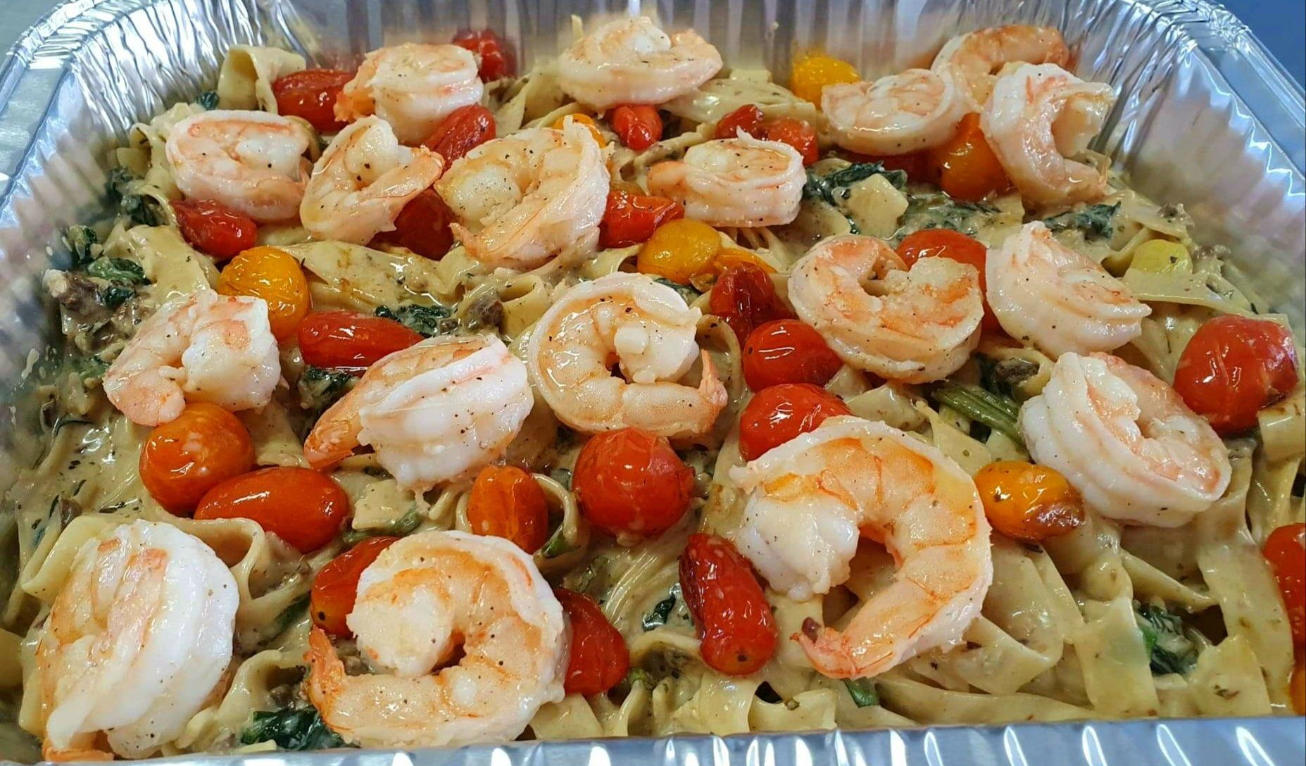 Una sartén de pasta con camarones, tomates y espinacas.
