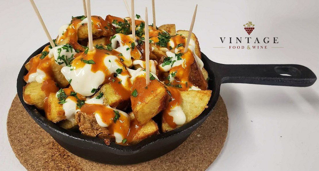 Una sartén llena de patatas cubiertas con salsa y queso en palillos.