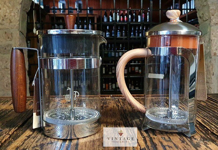 Dos cafeteras de prensa francesa con mangos de madera sobre una mesa de madera