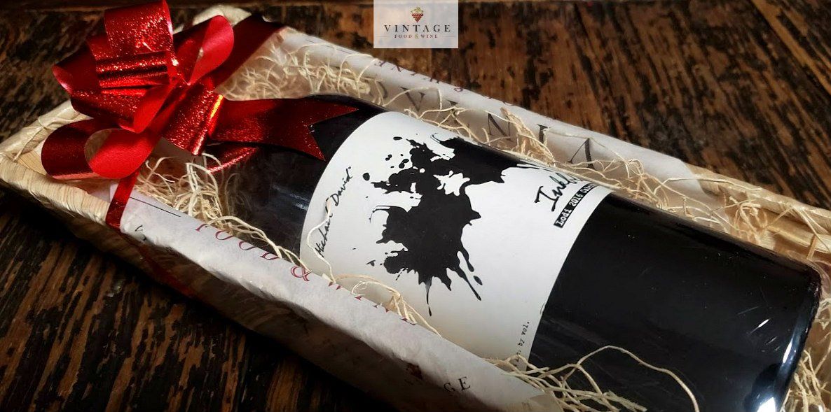 Una botella de vino en una caja de regalo con un lazo rojo.