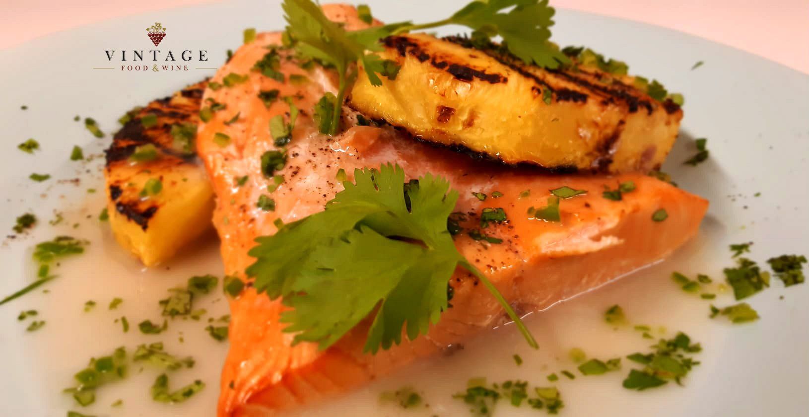 Un plato blanco cubierto con salmón a la parrilla y rodajas de piña.