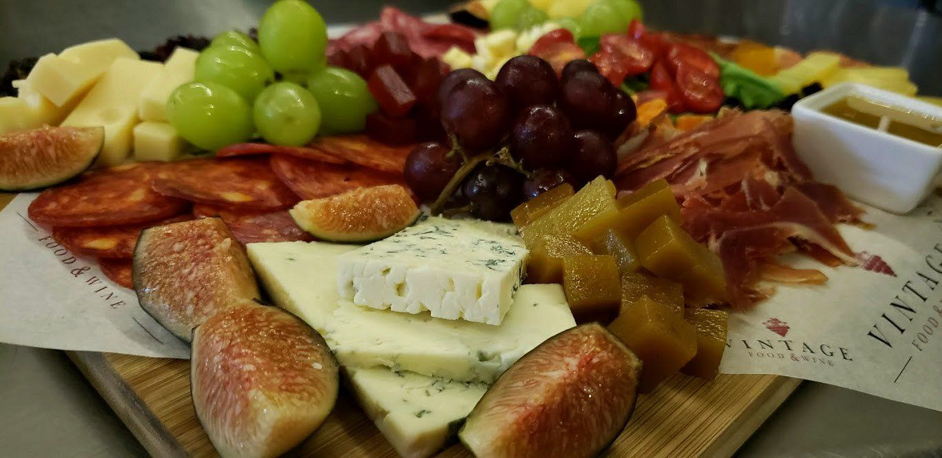 Una tabla de cortar de madera cubierta con queso, fruta y carne.