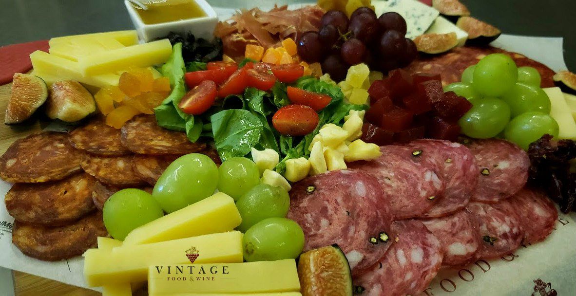 Un plato de comida con carne, queso, uvas y verduras sobre una mesa.