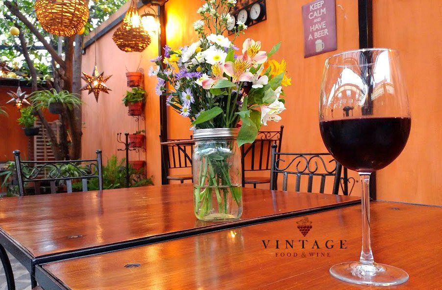 Una copa de vino reposa sobre una mesa junto a un jarrón de flores.