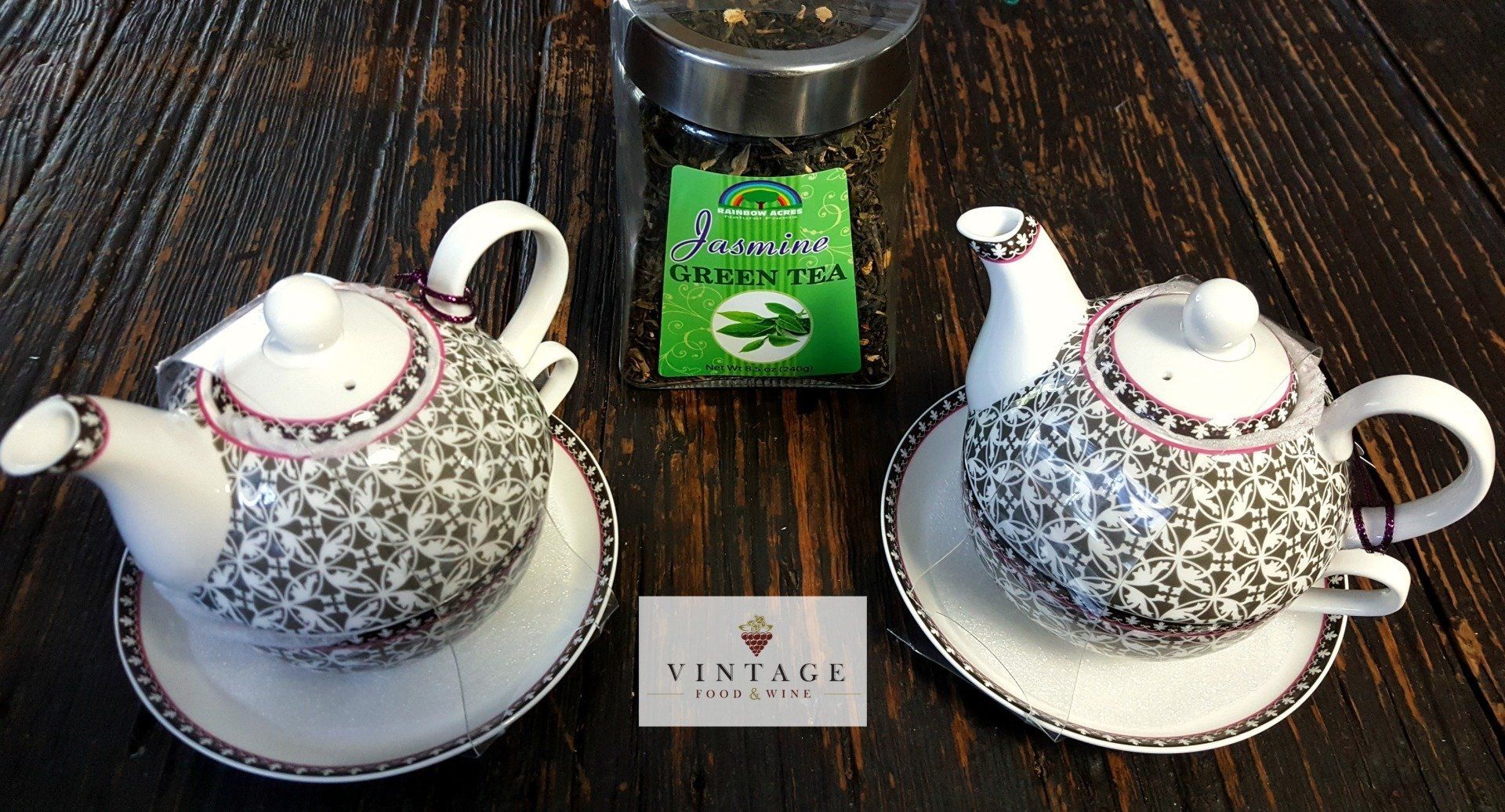 Dos teteras se encuentran sobre una mesa de madera junto a un frasco de té verde.