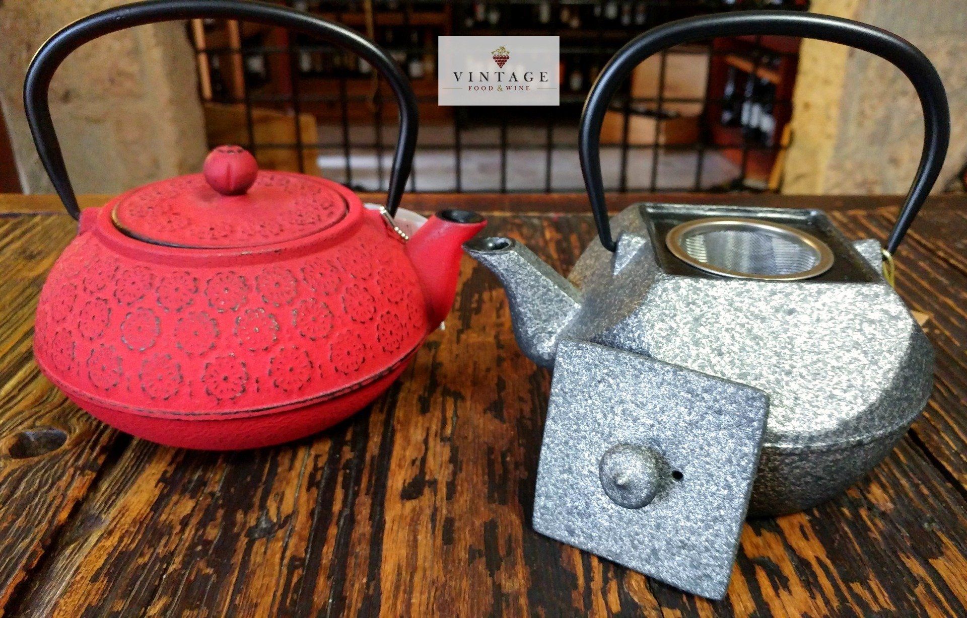 Una tetera roja y una tetera plateada están sobre una mesa de madera.