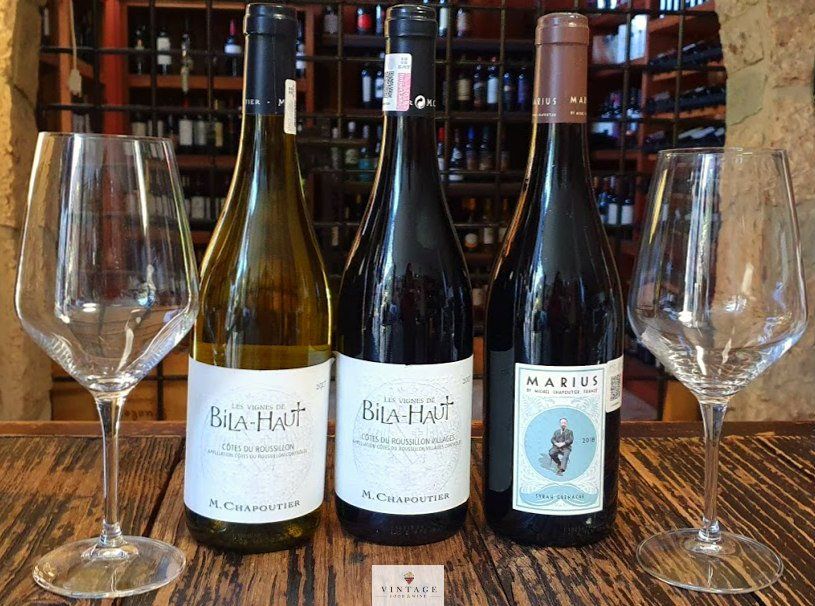 Tres botellas de vino y dos copas de vino en una mesa de madera.