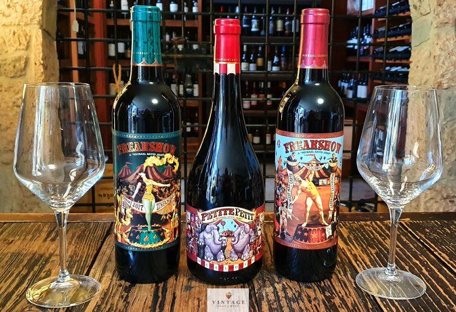 Tres botellas de vino y dos copas de vino en una mesa de madera.