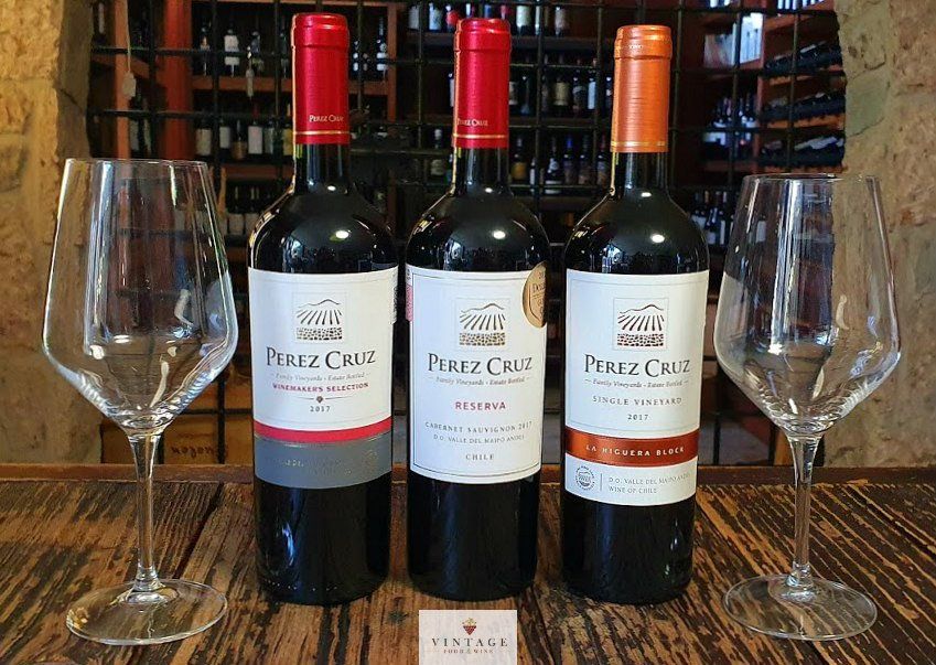 Hay tres botellas de vino sobre una mesa de madera al lado de dos copas de vino.