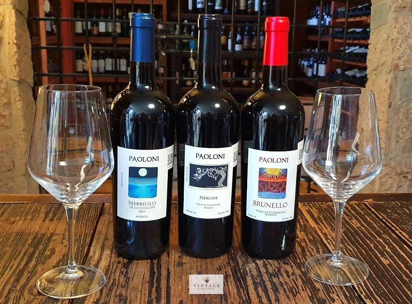 Tres botellas de vino y dos copas de vino en una mesa de madera.