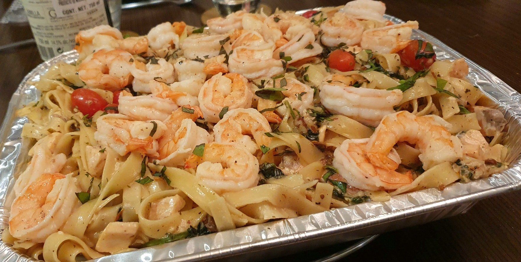 Una sartén de pasta con camarones y tomates sobre una mesa.