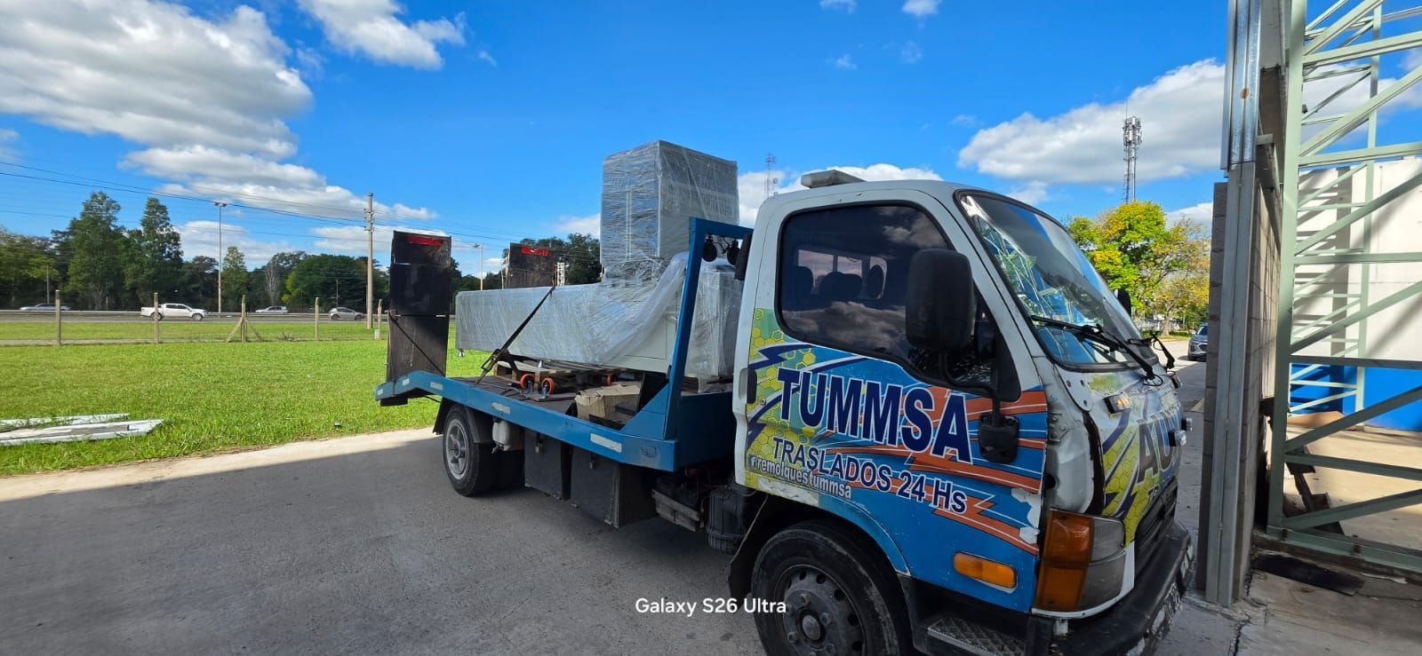 Un pequeño camión azul con plataforma de carga estacionado al borde de una carretera cubierta